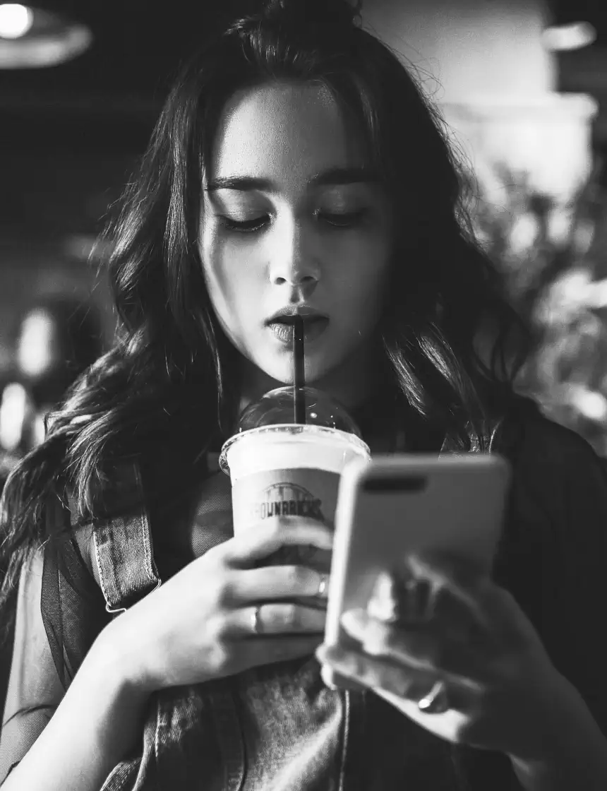 Young woman looks at phone while drinking coffee